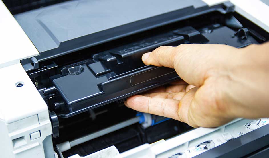 Een hand plaatst een toner in een printer. Het merk van de printer is niet zichtbaar op de foto.