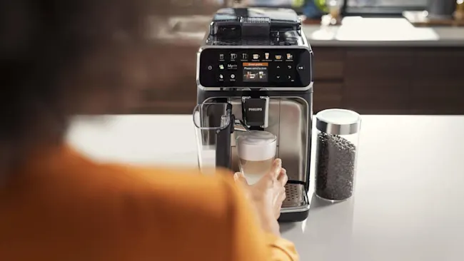 Een Philips koffiemachine schenkt koffie in een glas. Naast de machine staat een glazen pot met koffiebonen.