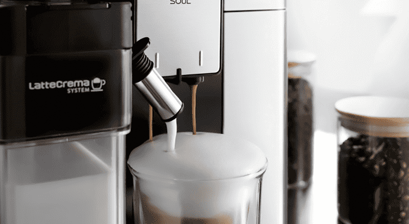 Een koffiemachine vult een glas met koffie en melkschuim, met koffiebonen op de achtergrond.