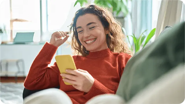 Lachende persoon op de bank kijkt naar een gele smartphone.