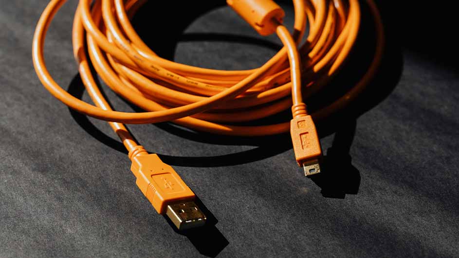 Een oranje USB-kabel ligt op een donkere ondergrond, opgerold in een lus met de uiteinden uitgestrekt.
