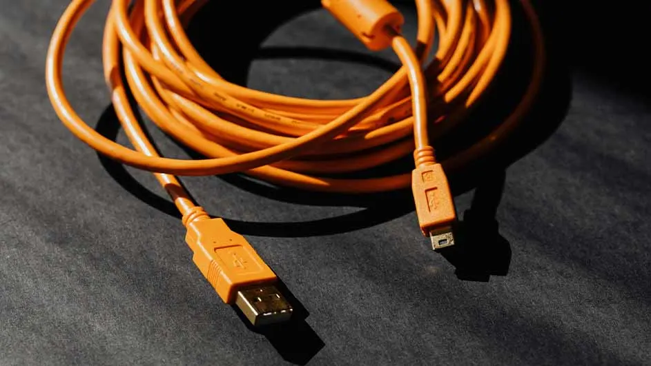Een oranje USB-kabel ligt op een donkere ondergrond, opgerold in een lus met de uiteinden uitgestrekt.