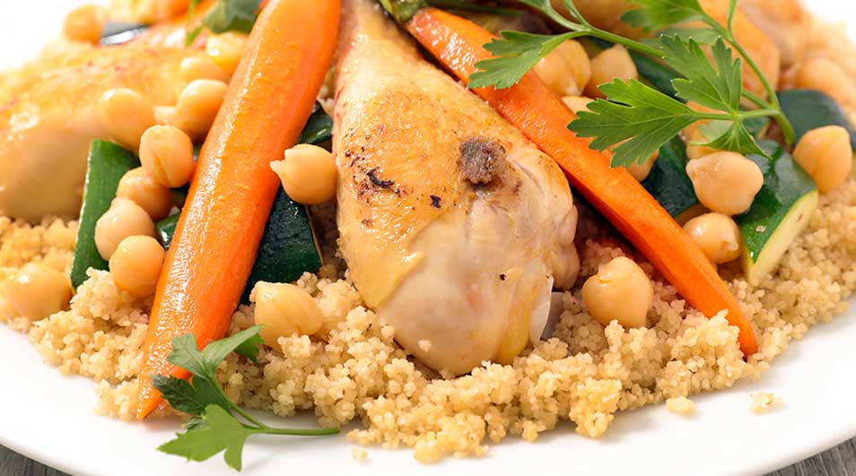 Een bord couscous met kip, wortelen, kikkererwten, courgette en peterselie.