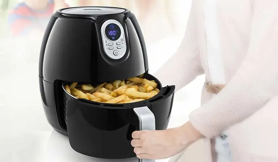 A woman takes chips out of a black Princess air fryer with digital display at 180°C. The air fryer sits on a white table.