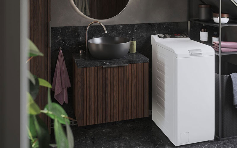 Moderne badkamer met houten wastafelmeubel, zwarte waskom en witte bovenlader wasmachine op donkere marmeren vloer.