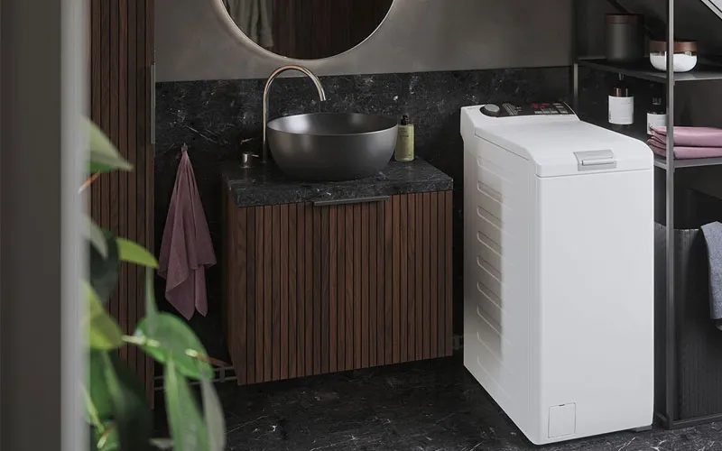 Moderne badkamer met houten wastafelmeubel, zwarte waskom en witte bovenlader wasmachine op donkere marmeren vloer.