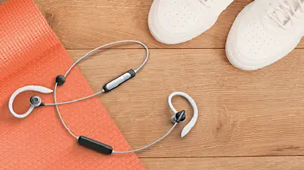 Witte sportschoenen, een oranje yogamat en witte oordopjes liggen op een houten vloer.