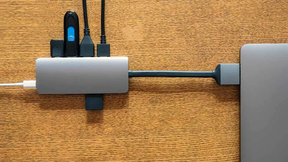Een grijze USB-hub is aangesloten op een laptop met kabels en een USB-stick tegen een houten achtergrond.