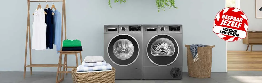 Twee moderne wasmachines in een lichte kamer, met opgevouwen was, planten en kleding op een rek zorgen voor een georganiseerde sfeer.