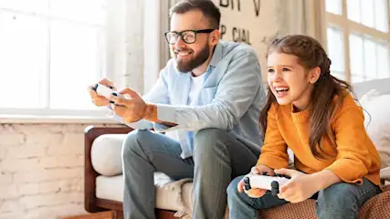 Een man met een bril en een meisje met een oranje trui spelen een computerspel met witte controllers.