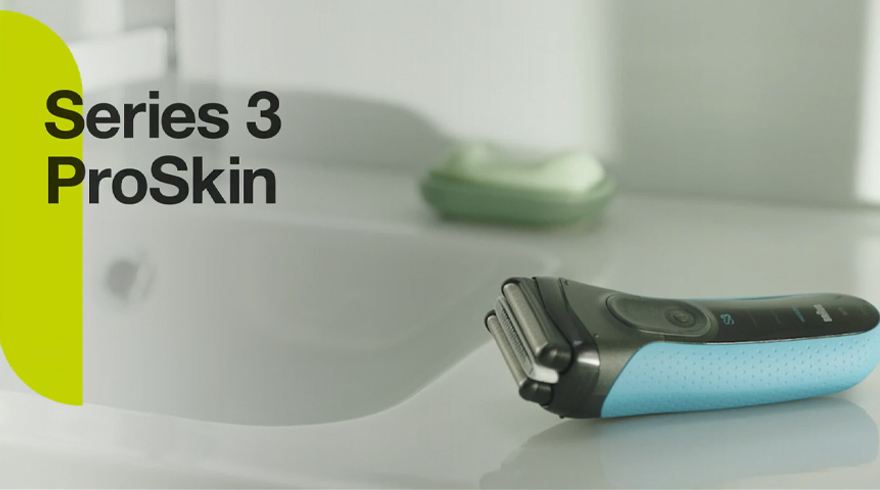 Een blauw-zwart scheerapparaat ligt op een wit oppervlak naast een witte wastafel met groene zeep.