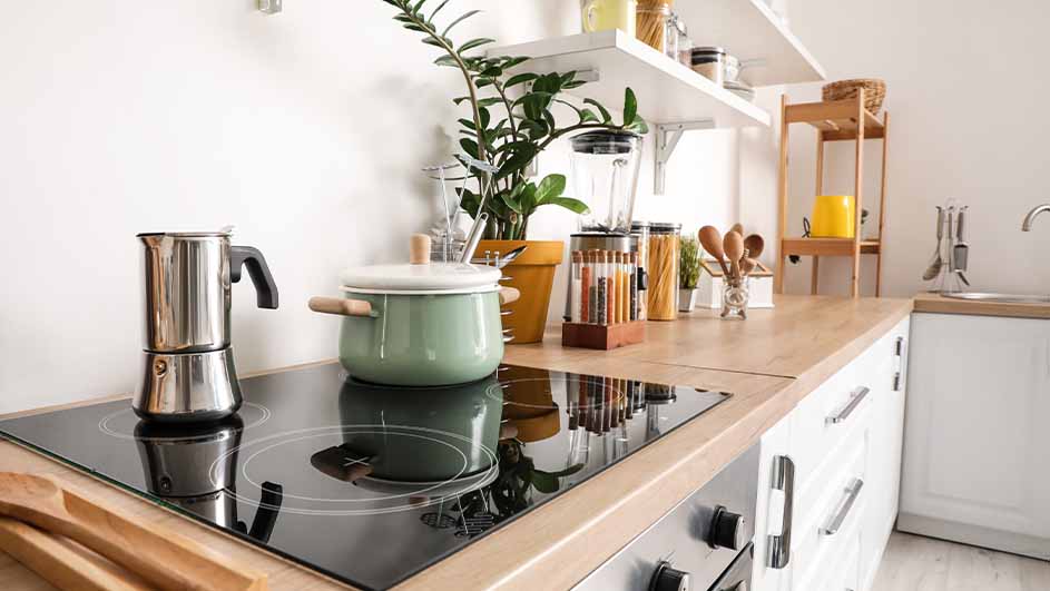 Een keuken met een kookplaat met een zilveren koffiezetapparaat en een groene pan. Er staan spullen op het aanrecht.