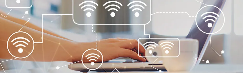 Een hand typt op een laptop naast een witte mok; overal zweven wifi-symbolen als digitale overlay. Merk is niet zichtbaar.