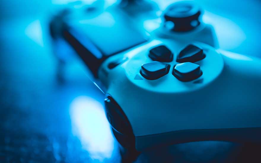 Close-up shot of a white PlayStation controller illuminated by blue light, highlighting the buttons and shiny finish.