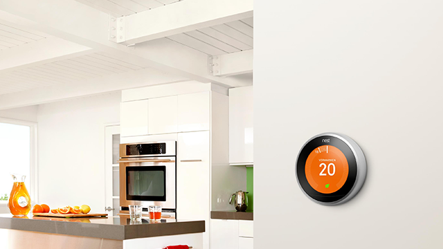 Moderne keuken met witte kasten, aanrecht met fruit en een Nest thermostaat op de witte muur, die 20 graden aangeeft.