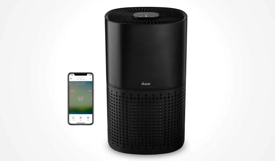 Black cylindrical Duux air purifier with perforated lower section and smartphone displaying air quality app on white background.