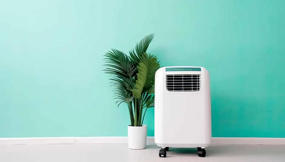 Een witte mobiele airco staat naast een plant in een witte pot tegen een turquoise achtergrond.