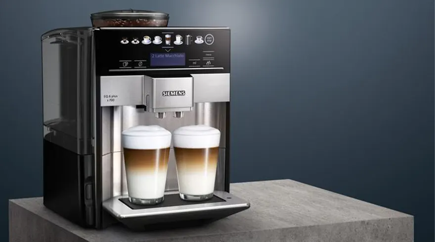Een Siemens koffiemachine met twee glazen latte macchiato op een grijze ondergrond tegen een blauwe achtergrond.