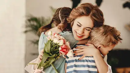 Een lachende vrouw omhelst twee kinderen en houdt een boeket tulpen vast. Het ene kind draagt een gestreept shirt, het andere heeft vlechten.