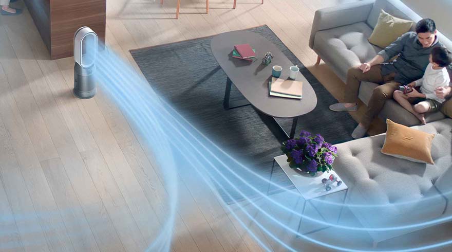 Woonkamer met een ventilator die blauwe luchtstroom produceert, een grijze tafel en een bank waarop een man en een kind zitten.