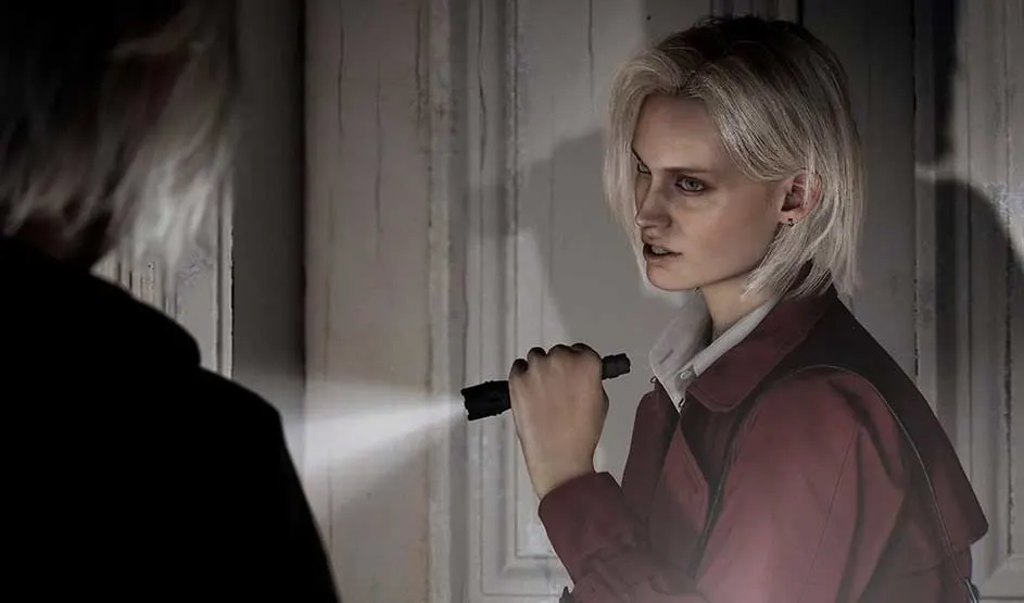 Dit is een videogame: blonde vrouw met zaklamp schijnt langs een houten deur en kijkt gespannen naar een schaduwfiguur op de voorgrond.