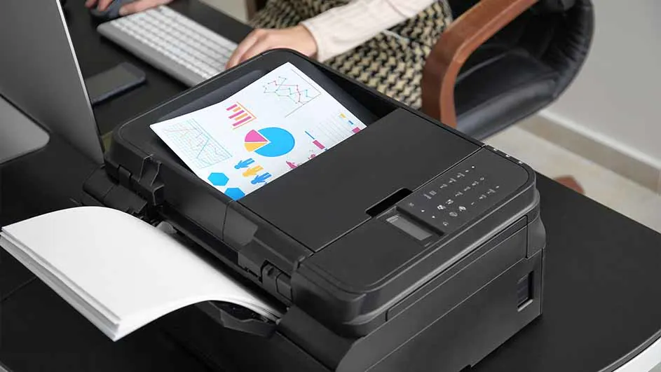 Een zwarte printer op een bureau print een vel papier met een cirkeldiagram en een lijngrafiek. Een toetsenbord is zichtbaar.