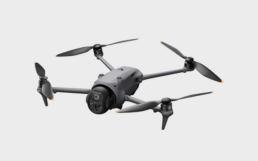 A dark grey drone with four propellers is shown diagonally against a light background, ready for take-off. 