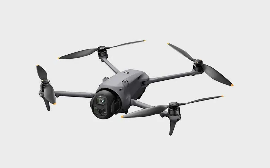 A dark grey drone with four propellers is shown diagonally against a light background, ready for take-off.