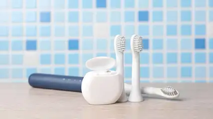 Twee witte elektrische tandenborstels, een blauwe houder en witte flosdraad tegen een achtergrond van blauwe tegels.