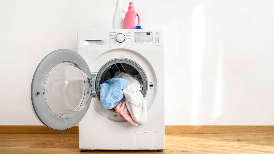 A white washing machine with an open door is filled with laundry. Two detergent bottles sit on top of the machine.