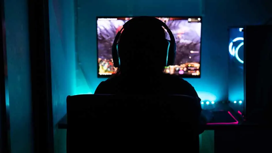 Donkere kamer met persoon met koptelefoon voor een computerscherm. Blauwe verlichting accentueert de randen van de schermen en de kamer.