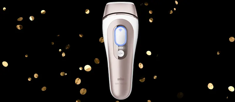 Op de afbeelding staat een Braun ontharingsapparaat met goudkleurige accenten, omringd door gouden confetti op een zwarte achtergrond.