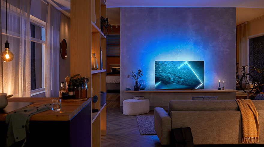 Woonkamer met televisie, bank, houten plank en blauwe verlichting. Er is een raam met gordijnen en een fiets op de achtergrond.