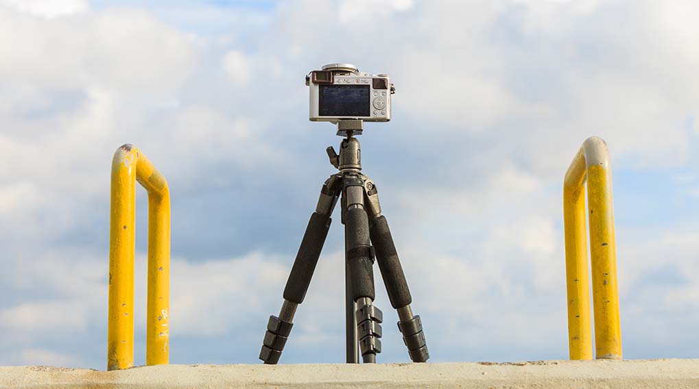 Een camera op een statief, met gele hekken aan de zijkanten tegen een bewolkte lucht.