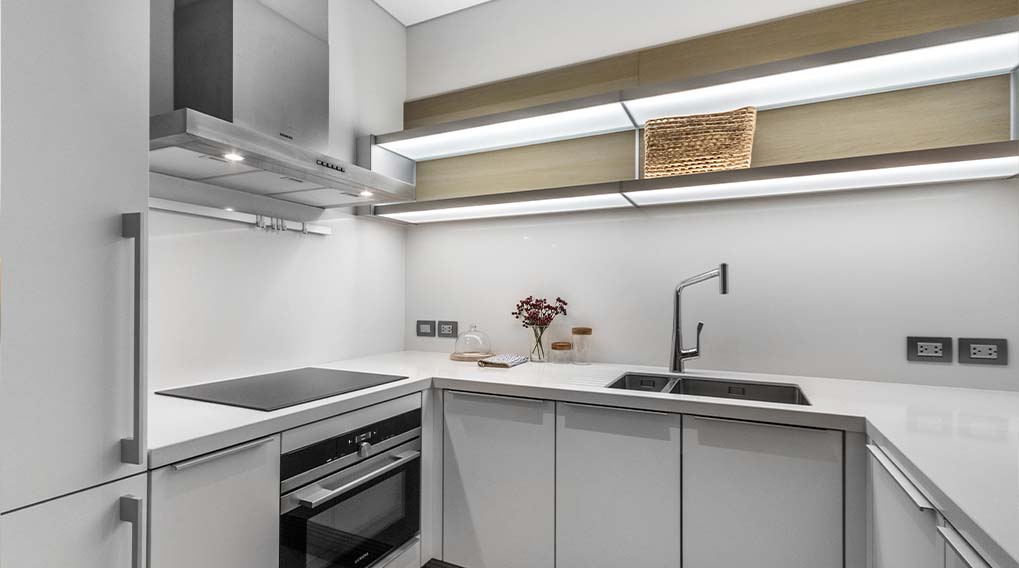 Moderne keuken met witte kasten, aanrecht, spoelbak, kookplaat en roestvrijstalen afzuigkap. Er is een houten mand op een plank.