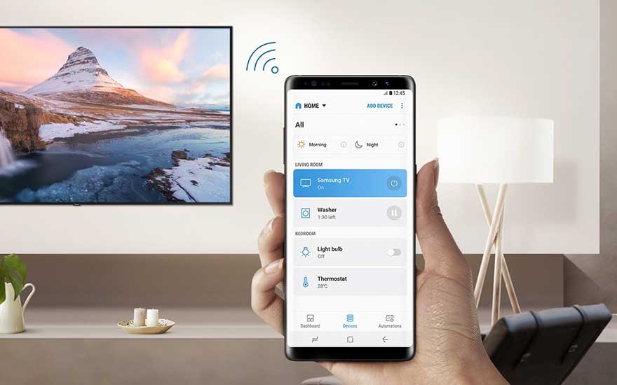 Smartphone toont smart home app met Samsung TV-bediening, thermostaat en verlichting in moderne woonkamer met berglandschap op TV-scherm.