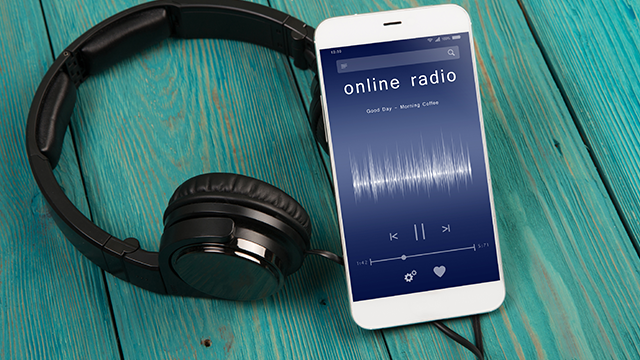 Zwarte hoofdtelefoon en witte telefoon op een blauwe houten ondergrond, met 'online radio' op het scherm.