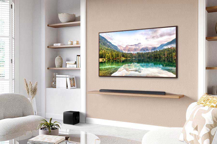 Een moderne woonkamer met een tv aan de muur die een berglandschap toont, een soundbar op een plank en een subwoofer op de grond.