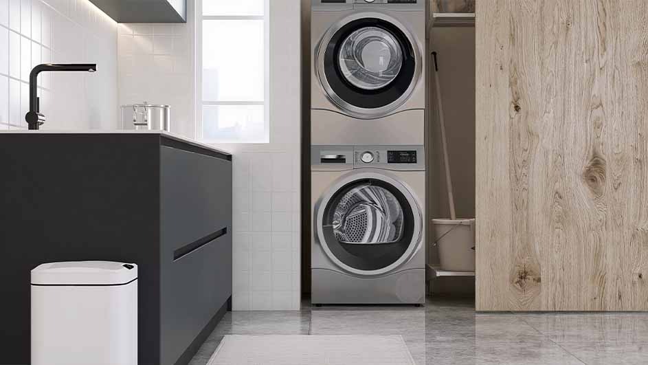 A laundry room scene features a stacked washer and dryer next to a dark cabinet and white trash can. A light wood door is visible.