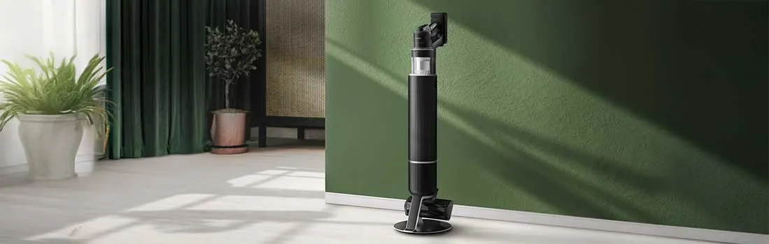 Een slanke zwarte steelstofzuiger staat op zijn laadstation tegen een diepgroene muur in een moderne, lichte woonkamer met plant.