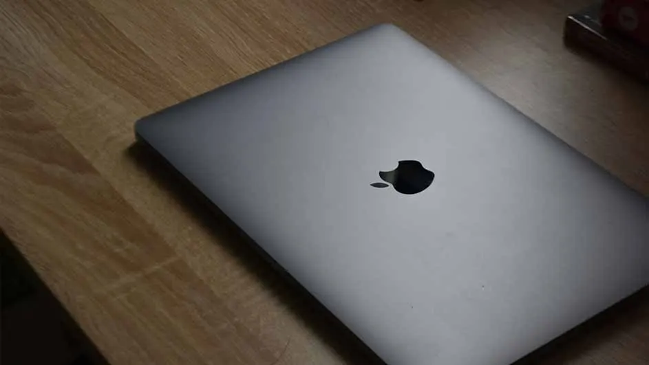 A closed silver laptop with a black apple logo sits on a wooden surface.