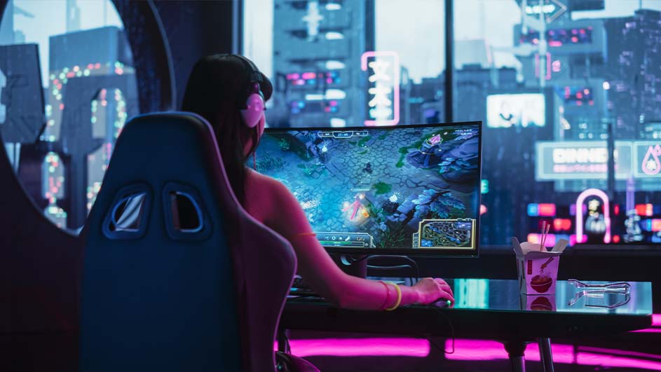 Een persoon zit op een stoel voor een computerscherm met een spel, voor een raam met een stadsgezicht.