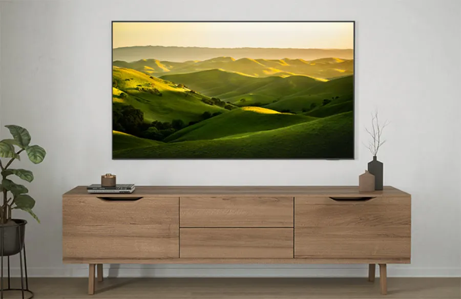 Houten dressoir met laden en decoratie, een plant links en een foto van heuvels aan de witte muur erboven.