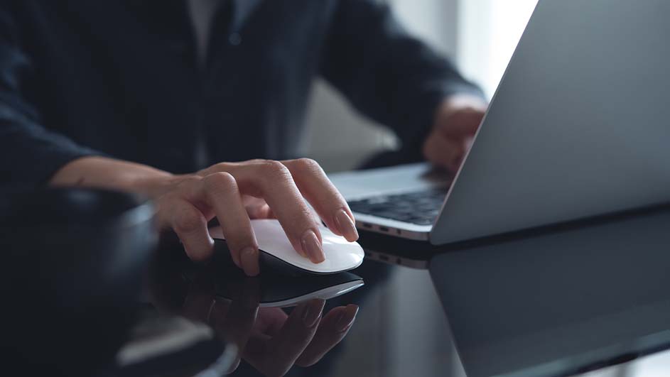 Een persoon gebruikt een witte en zwarte computermuis naast een grijze laptop op een glanzend zwart bureau.