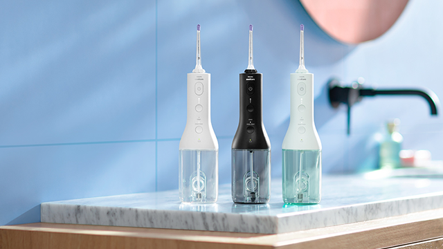 Drie waterflossers in wit, zwart en lichtgroen staan op een marmeren aanrecht in een badkamer.