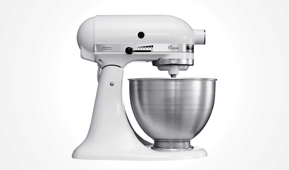Een witte KitchenAid Classic keukenmachine met metalen mengkom staat in profiel op een witte achtergrond; je ziet de snelheidshefboom en motorbehuizing.