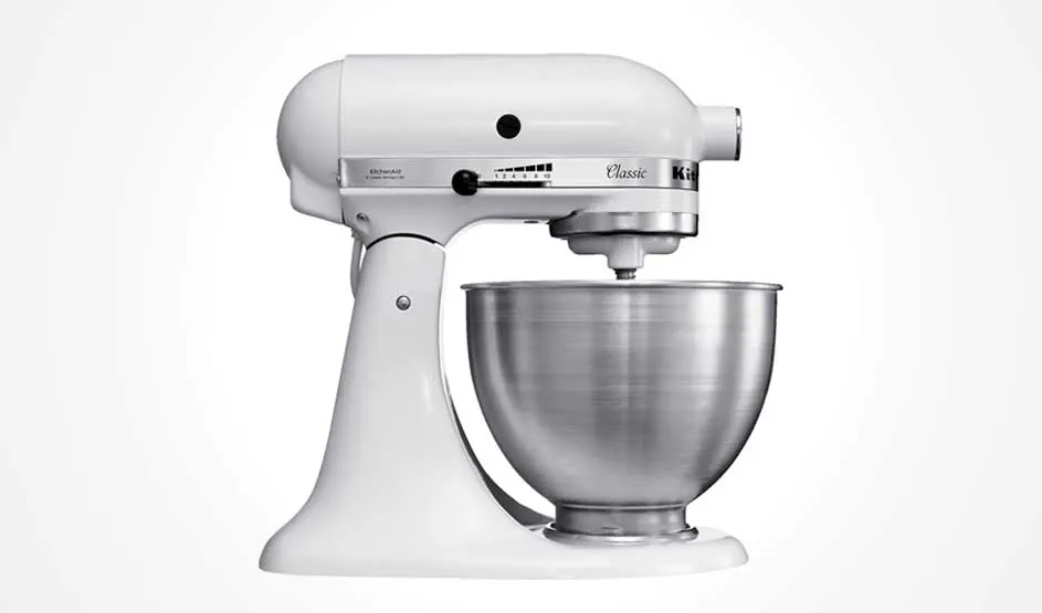 Een witte KitchenAid Classic keukenmachine met metalen mengkom staat in profiel op een witte achtergrond; je ziet de snelheidshefboom en motorbehuizing.