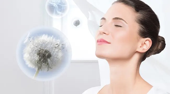 A woman closes her eyes and breathes in pure air as dandelion seeds drift in clear bubbles, suggesting allergens safely captured.