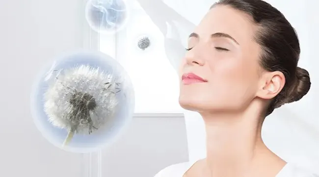 A woman closes her eyes and breathes in pure air as dandelion seeds drift in clear bubbles, suggesting allergens safely captured.