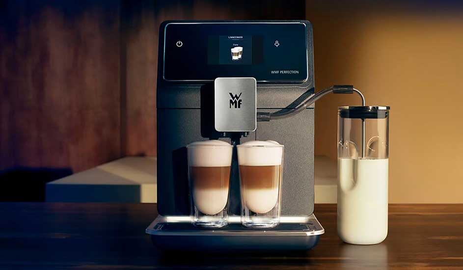Een moderne WMF koffiemachine maakt twee latte macchiato’s tegelijk, met een melkbeker en digitaal scherm op een houten aanrecht. 